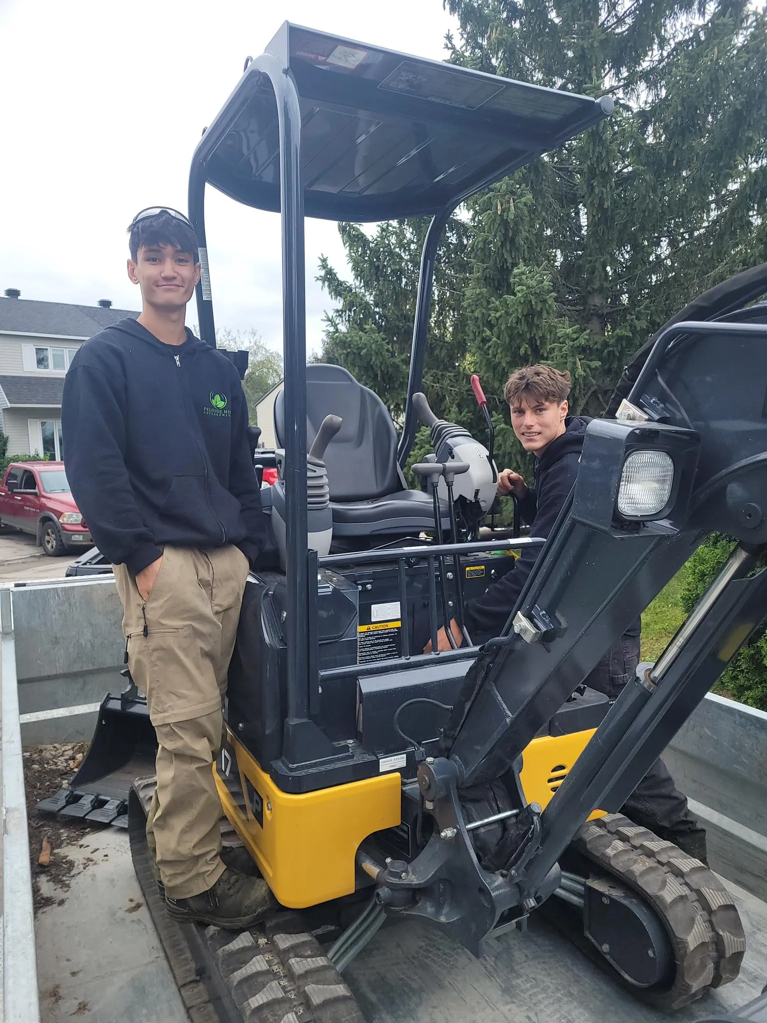 Deux employés de Pelouse Men Paysagement utilisant une mini-chargeuse compacte pour un projet d’aménagement.