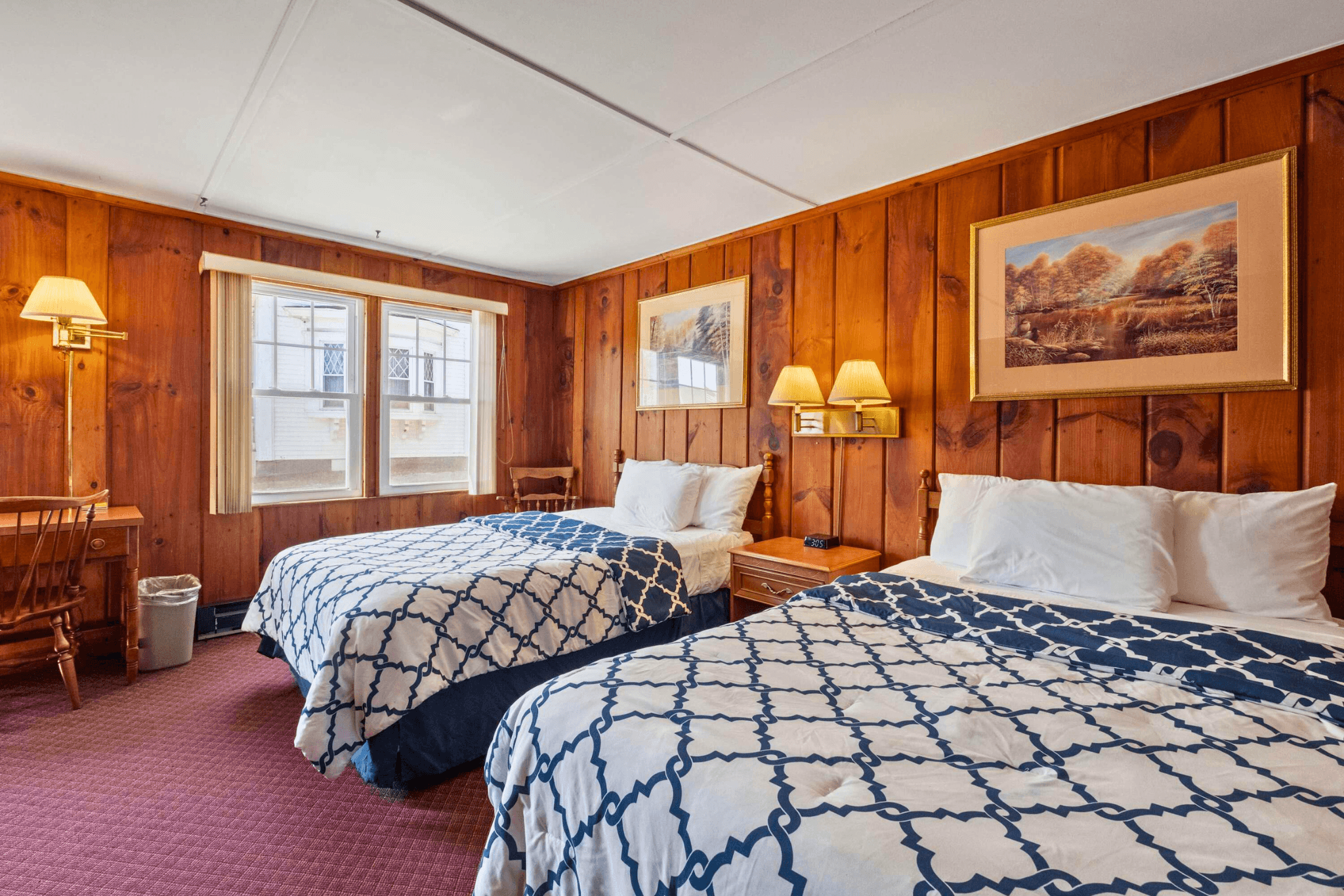 Warm, wood-paneled motel room with two queen beds, soft lighting, and classic decor offering comfortable accommodations in downtown Littleton, NH.