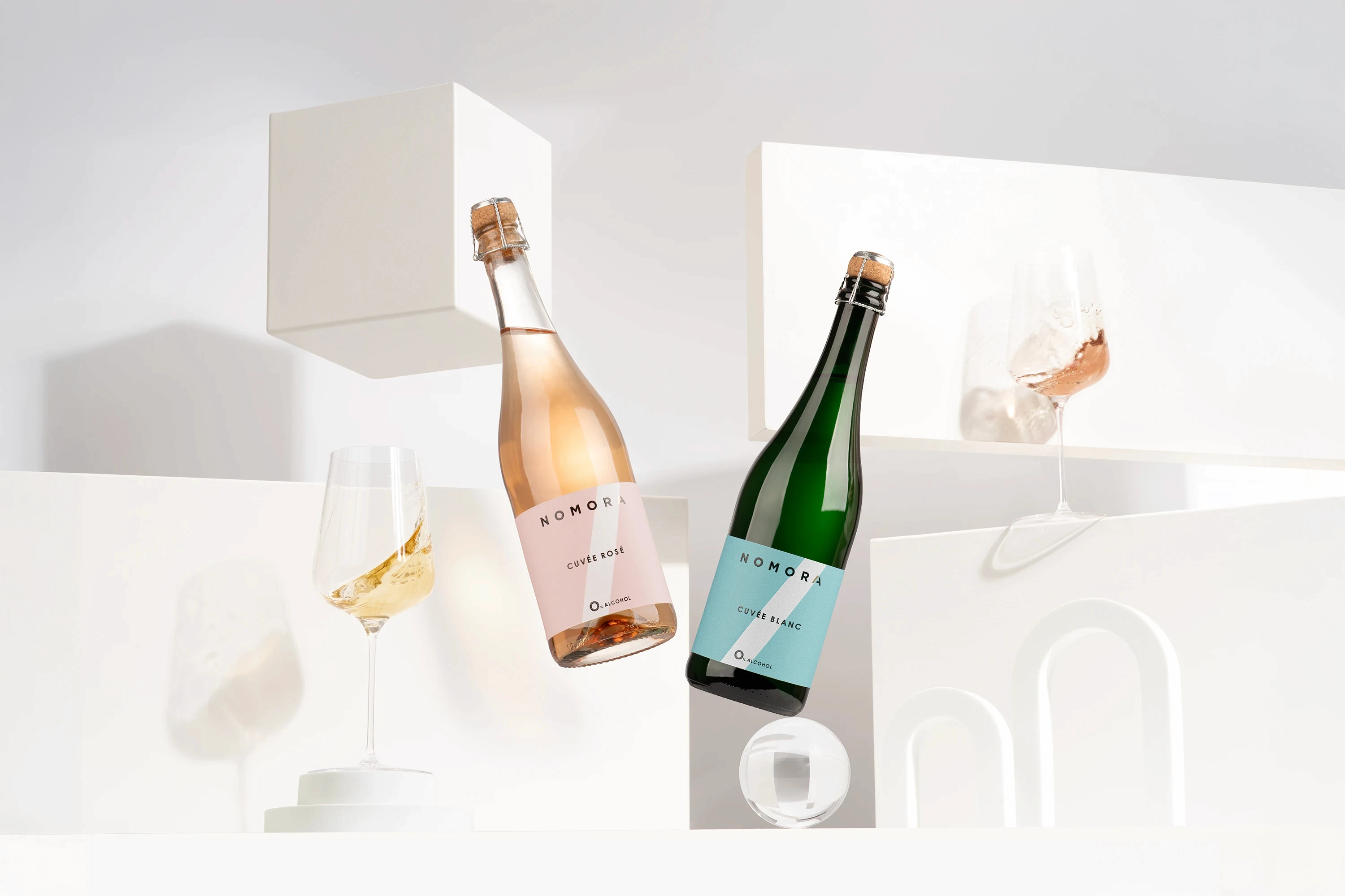 Two bottles of sparkling wine on a white surface, with elegant packaging in the background.