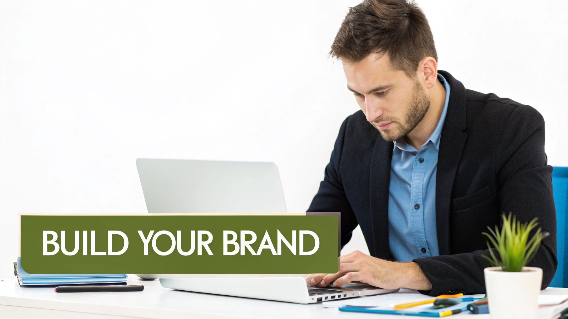 Professional man in a blazer working on a laptop, with a 'BUILD YOUR BRAND' sign.