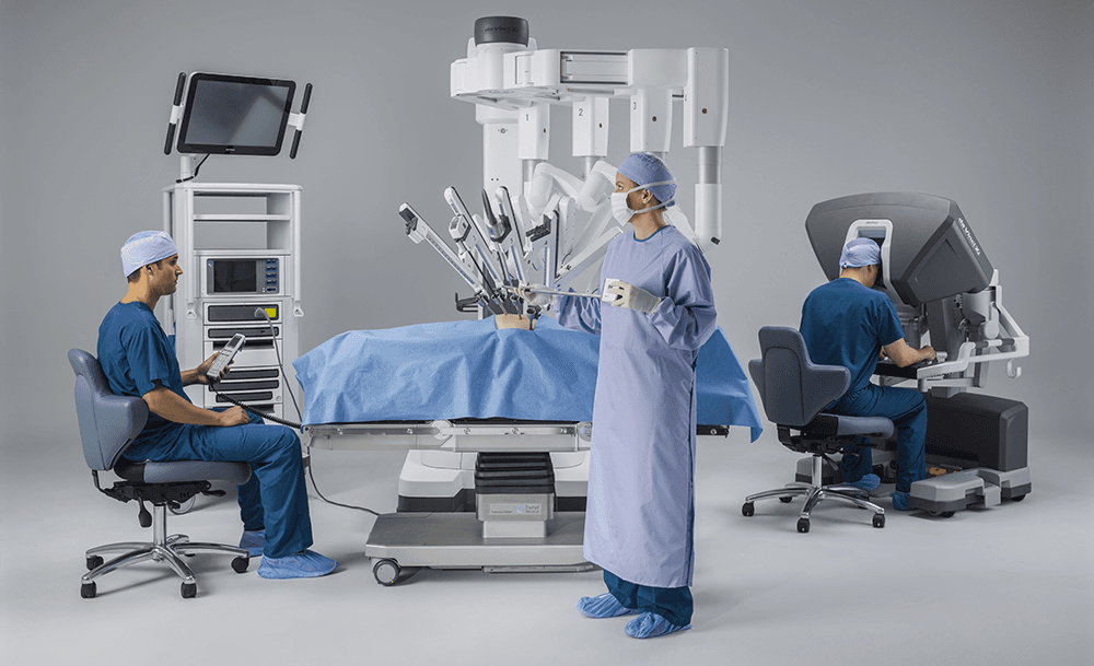 ऑपरेटिंग रूम में पूरा Da Vinci Xi robotic system दिखाया गया है, जिसमें surgeon console, patient-side cart, और vision cart शामिल हैं।