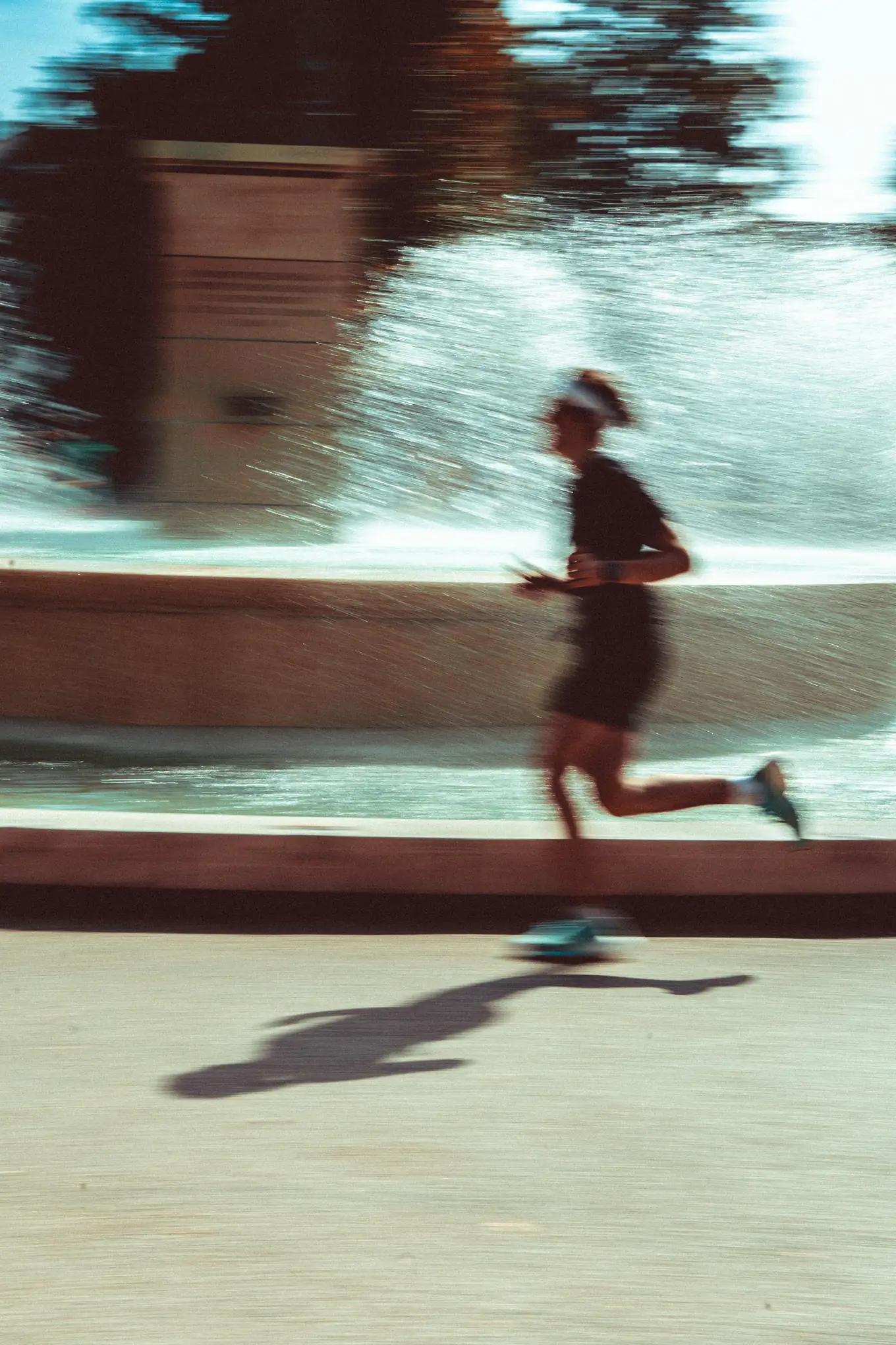 A runner passing a splashing fountain on a sunny day