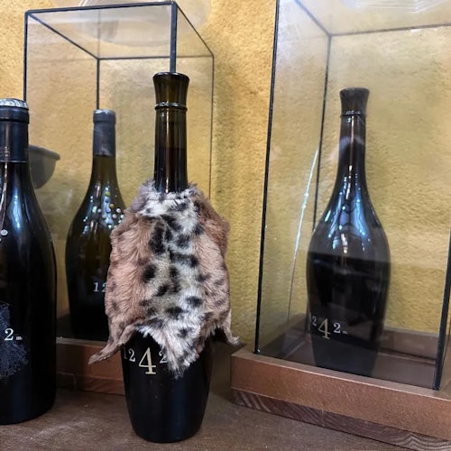 一个覆盖着动物毛皮的酒瓶在一个玻璃柜中展示，背景中有类似的酒瓶。