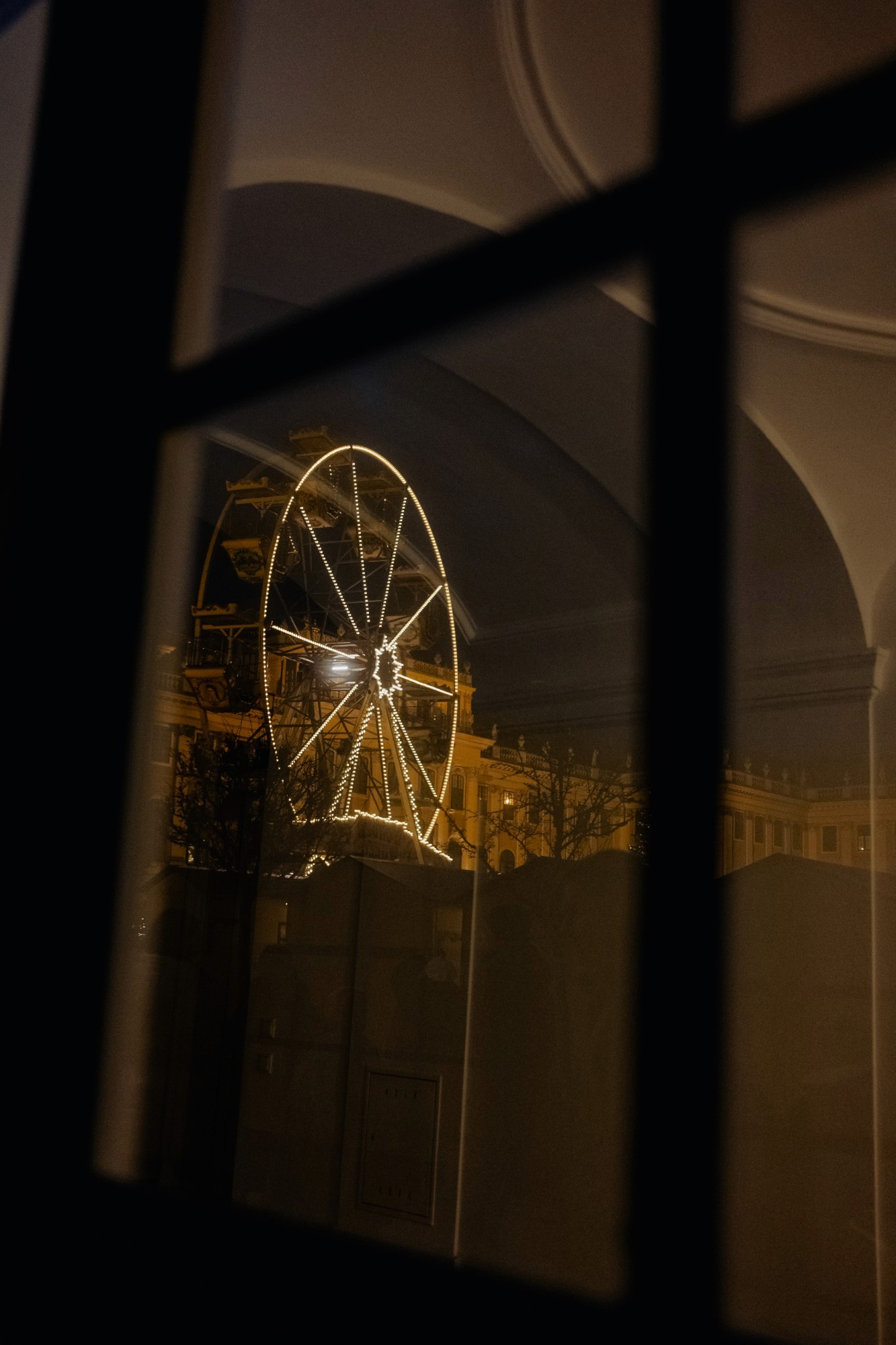 Reflejo en un cristal de la noria iluminada y el palacio de Schönbrunn