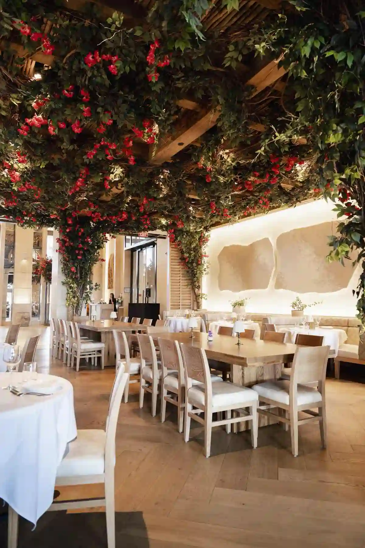 A stylish restaurant interior featuring elegant tables and chairs under a canopy of greenery and hanging decor.