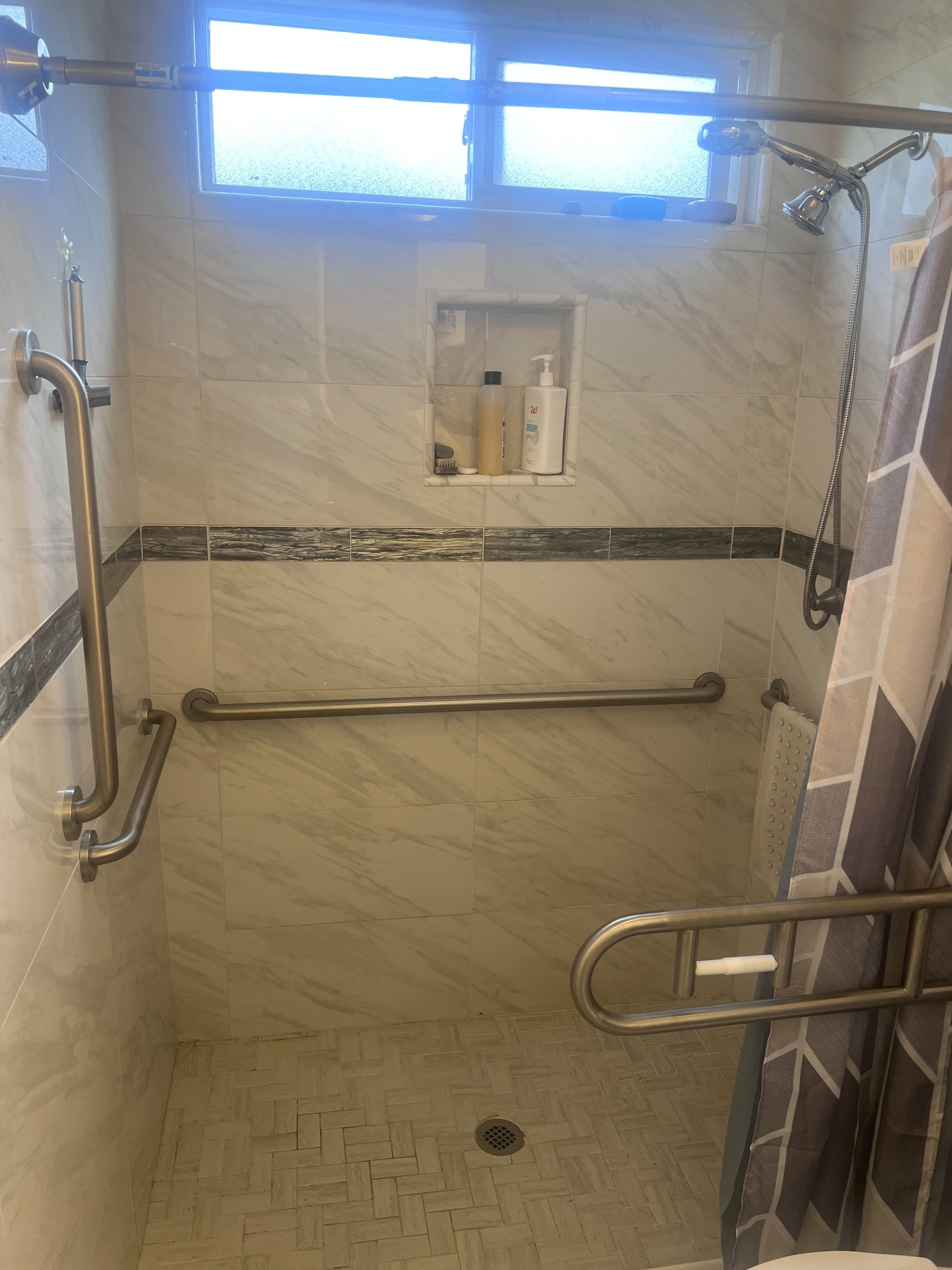 Tiled roll-in shower with long stainless grab bars and a handheld shower head