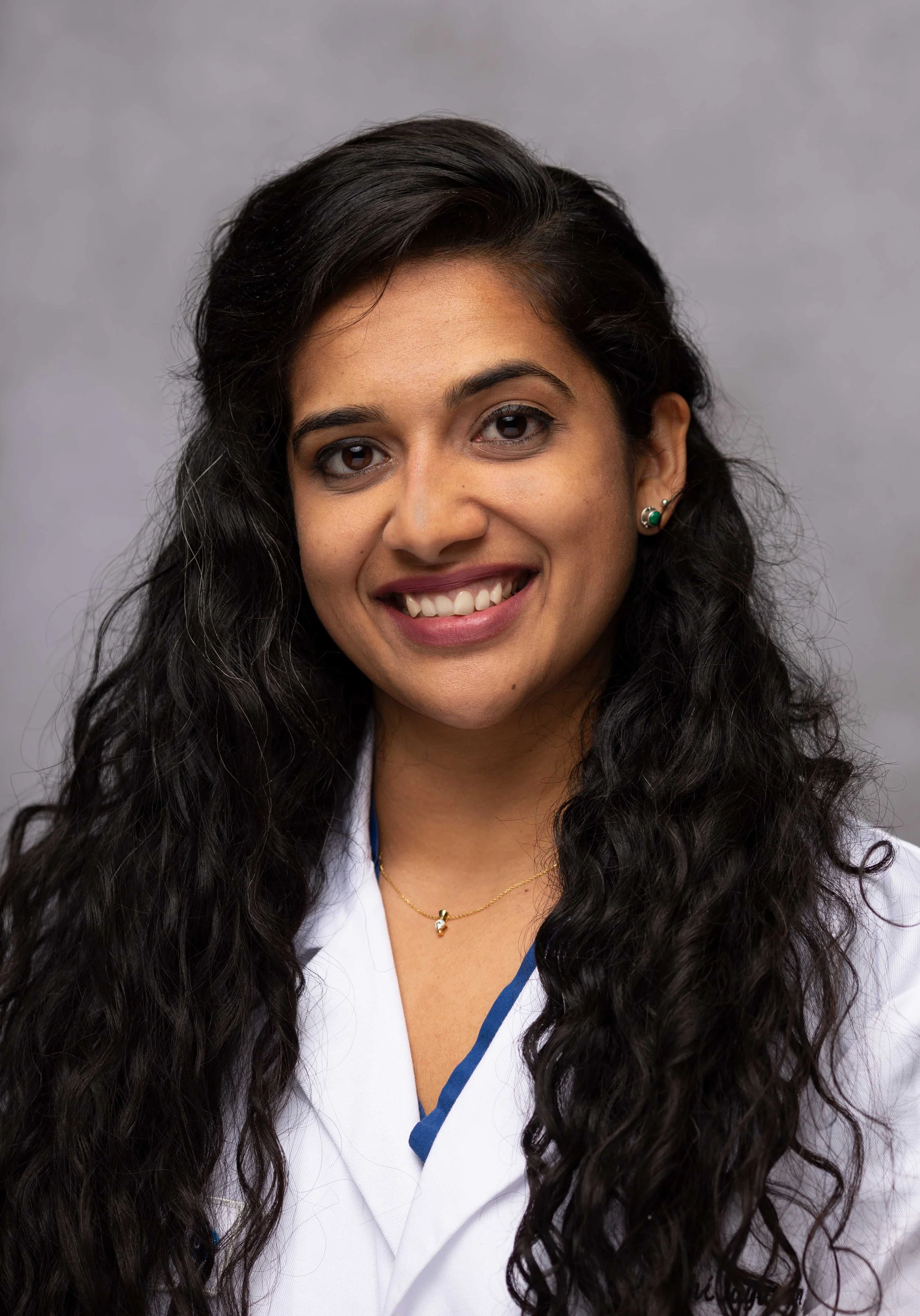 Woman in white lab coat smiling, grey background