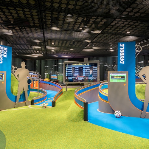 Indoor soccer-themed attraction with interactive stations for corner kick and dribble, featuring digital scoreboards and soccer balls.