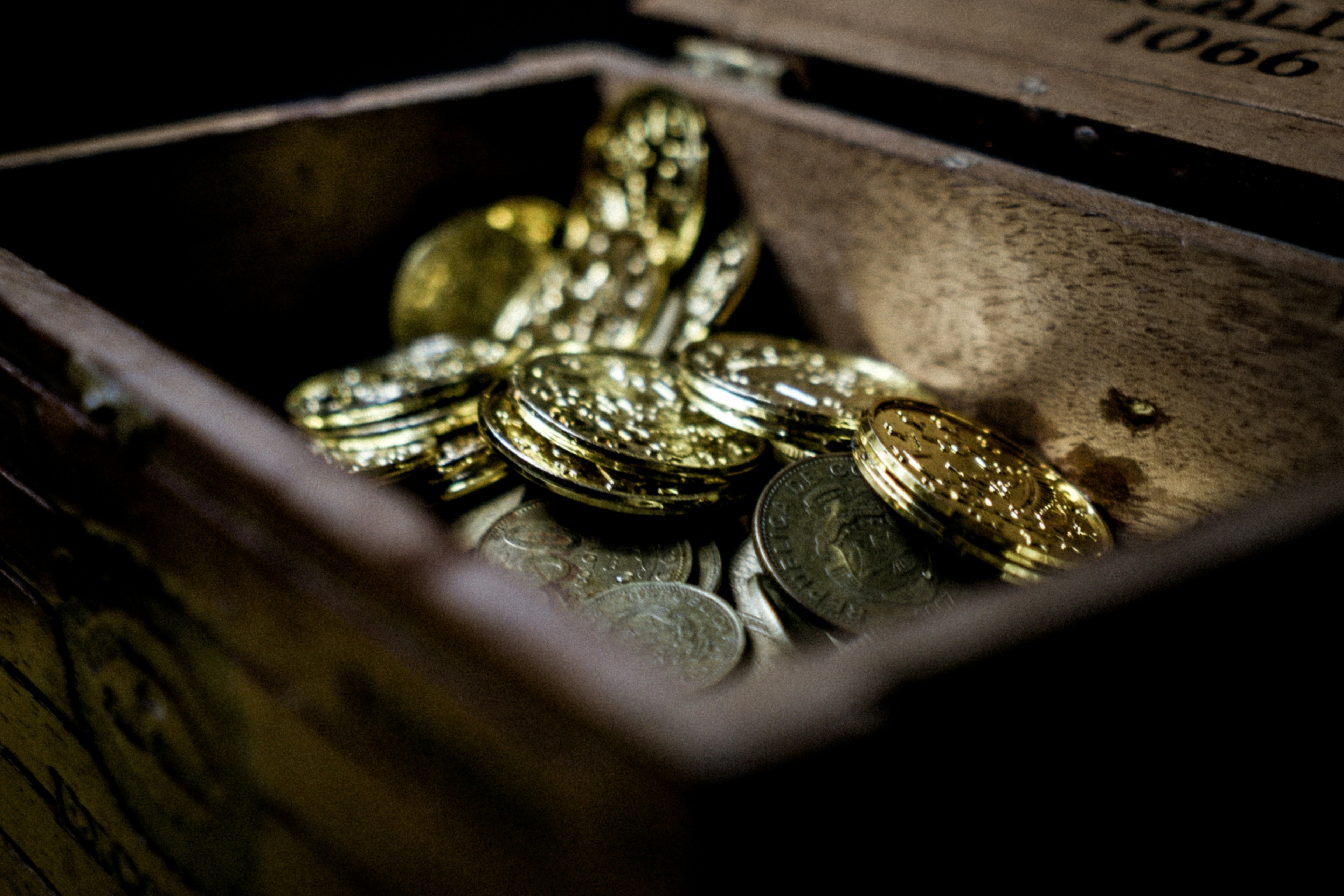 Wooden treasure chest filled with gold and silver coins, partially open to reveal the contents inside.