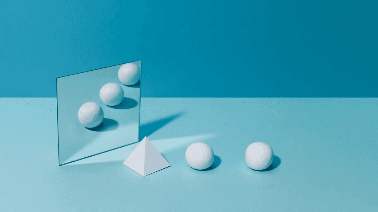 Two white spheres and a white pyramid sit on a blue surface. A mirror reflects three white spheres.