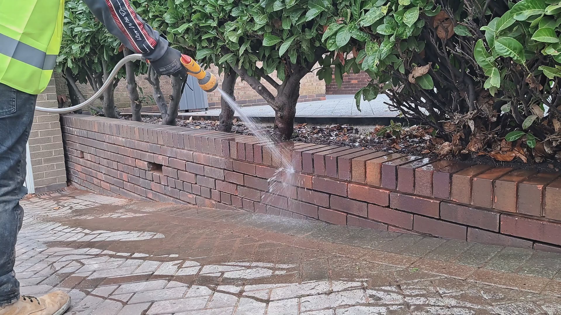 A man washing out brick joints of a garden wall