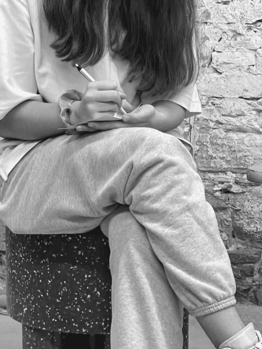 A person seated on a speckled stool, intently writing in a notebook. This scene embodies participative strategizing, highlighting the collaborative approach to developing actionable strategies.