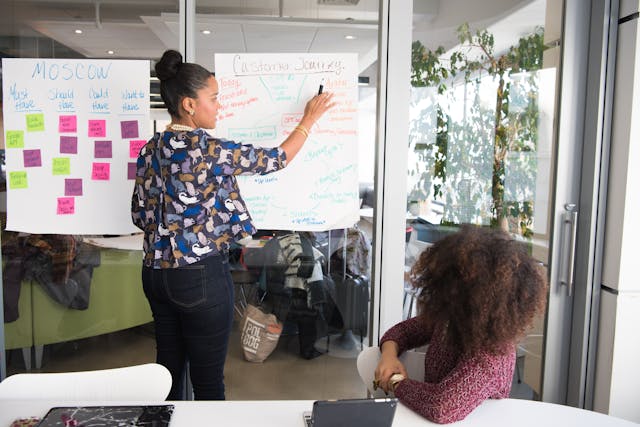A person pointing at a large sheet of paper stuck to a glass wall during a brainstorming session
