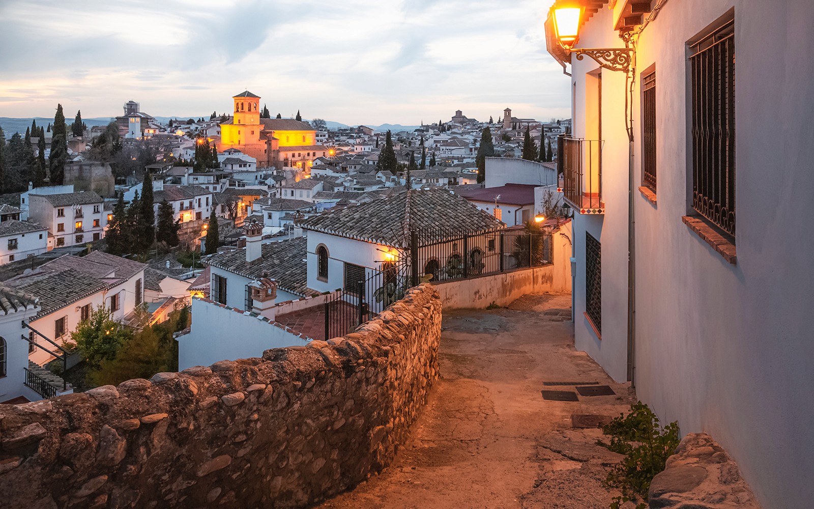 Alleyway in Albaicín, Granada, with illuminated historic buildings at dusk.