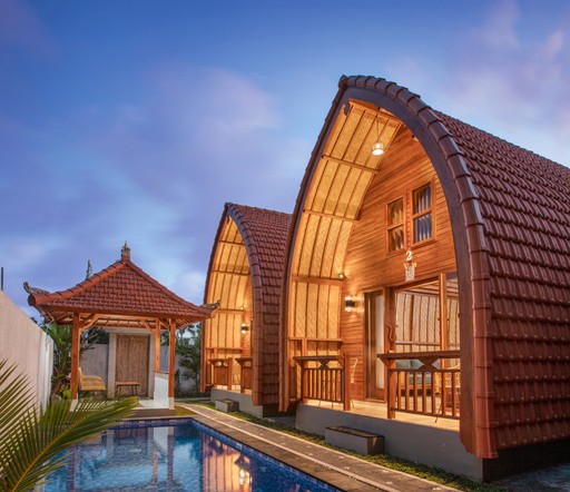 Smiling young woman with long hair standing against a dark green background, holding a finger to her chin.