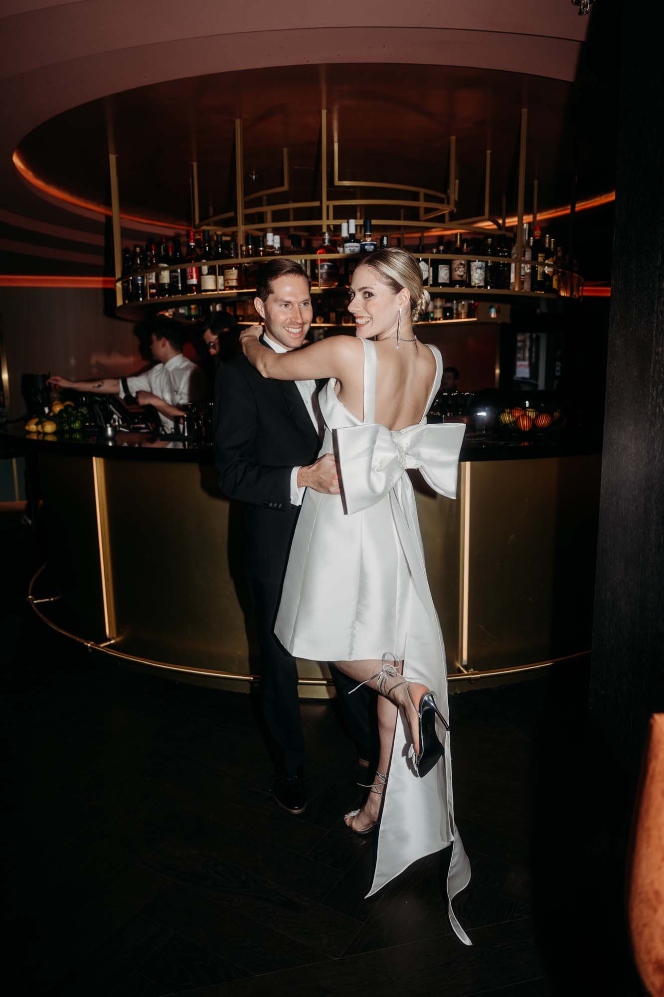 Brautpaar in einer Bar mit kurzem Kleid und einer riesen Schleife am Rücken.