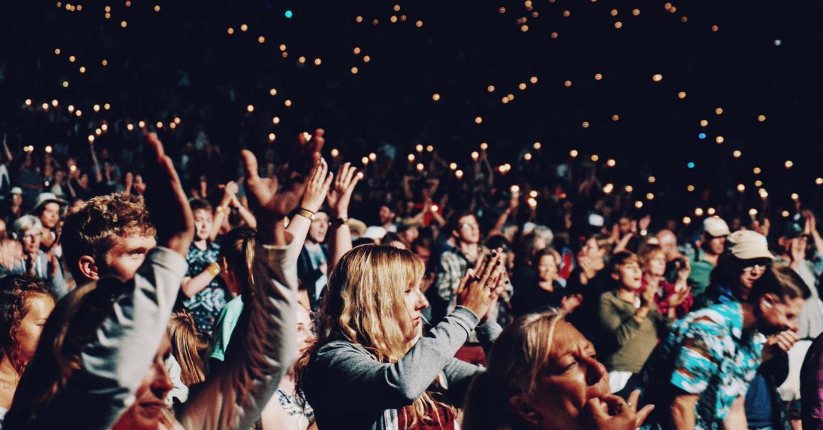 Crowd cheering at a lively concert with lights in the background.
