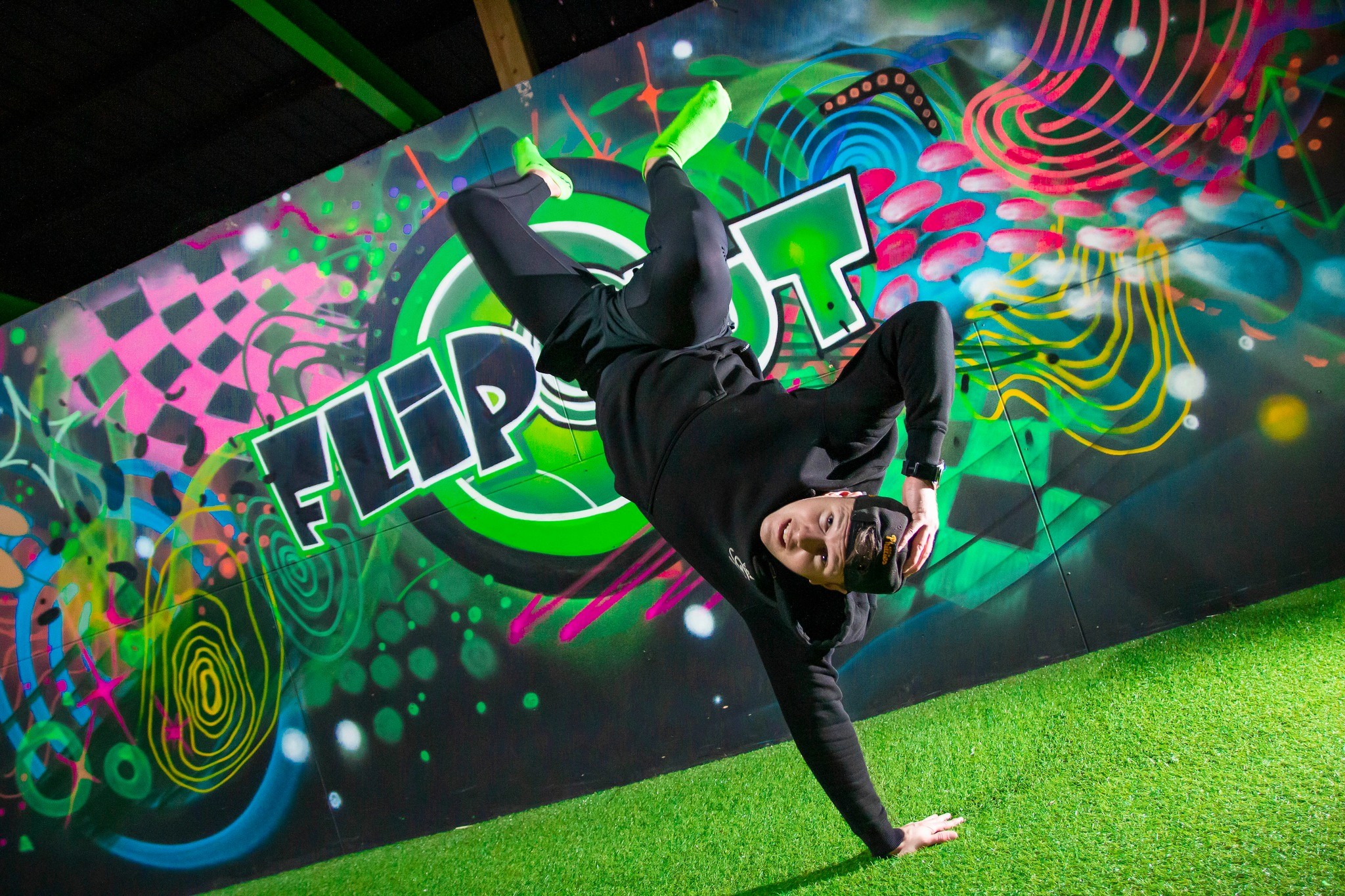 A breakdancer performs a headspin in front of a vibrant Flip Out mural.
