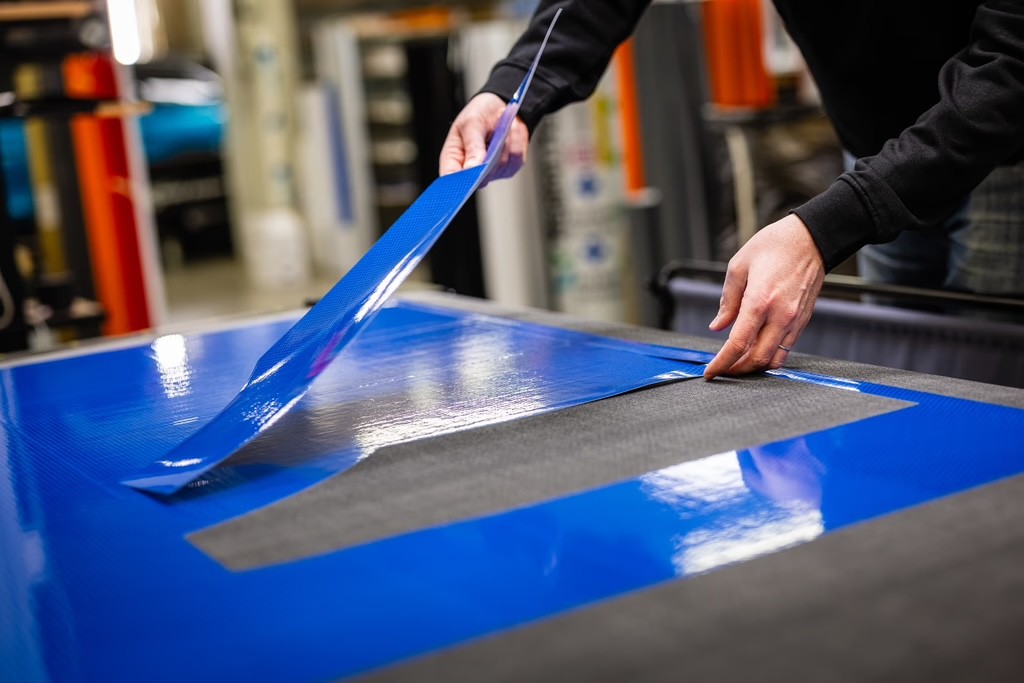 Medarbetare applicerar och skär blå folie på en stor yta, hantverk och precision.