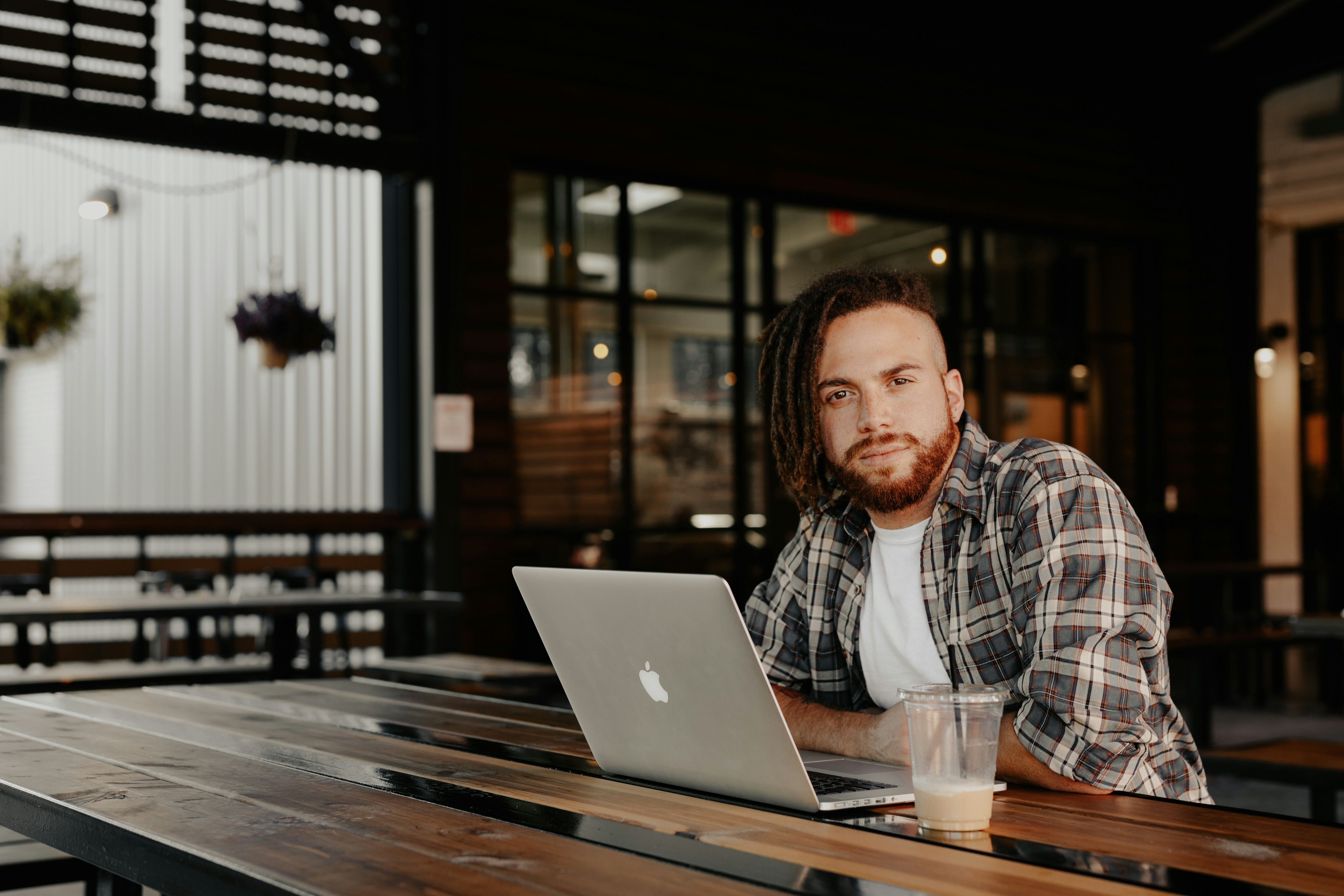 man in black and white plaid dress shirt sitting by the table using macbook