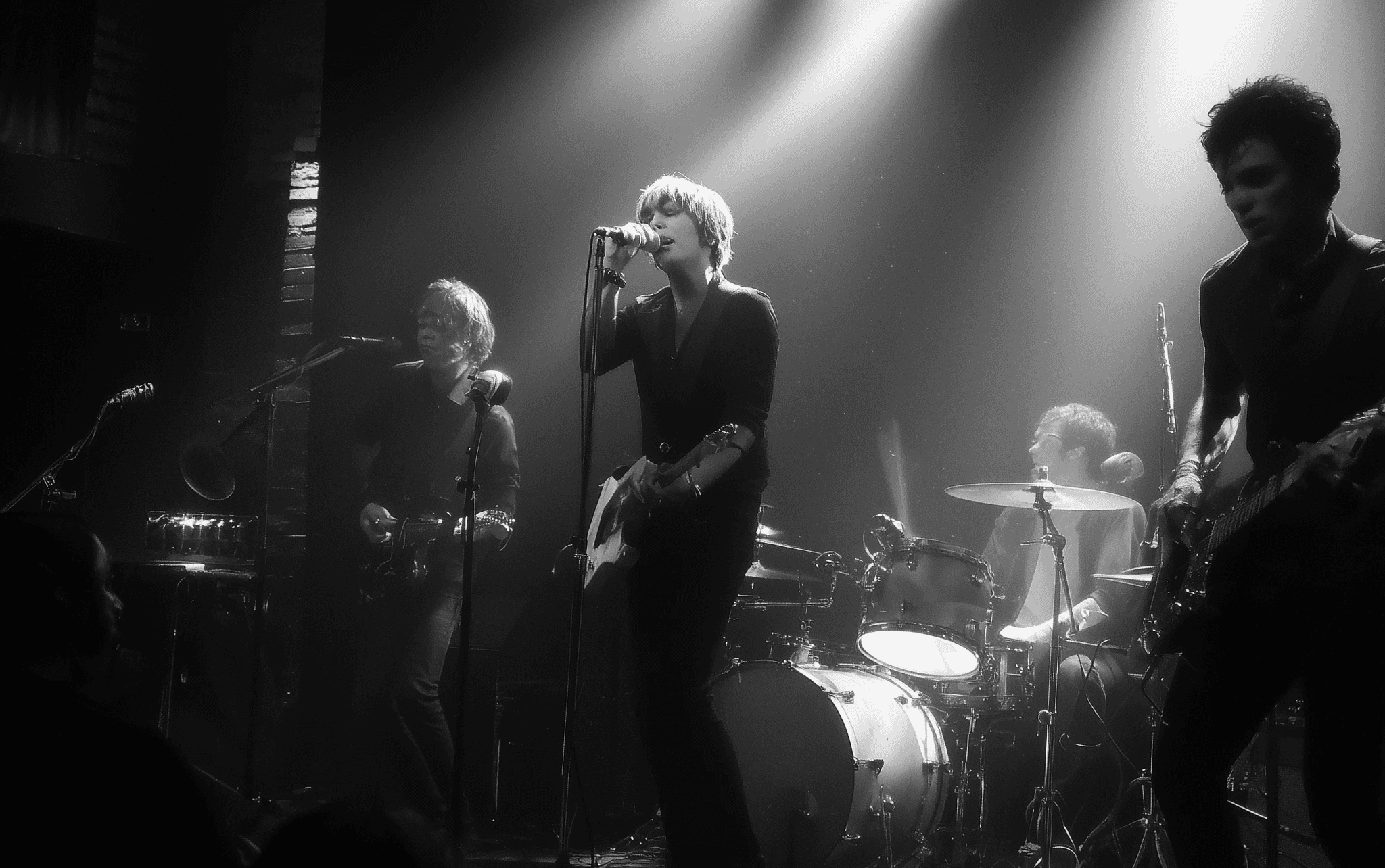 A black and white image of a rock band performing on stage.