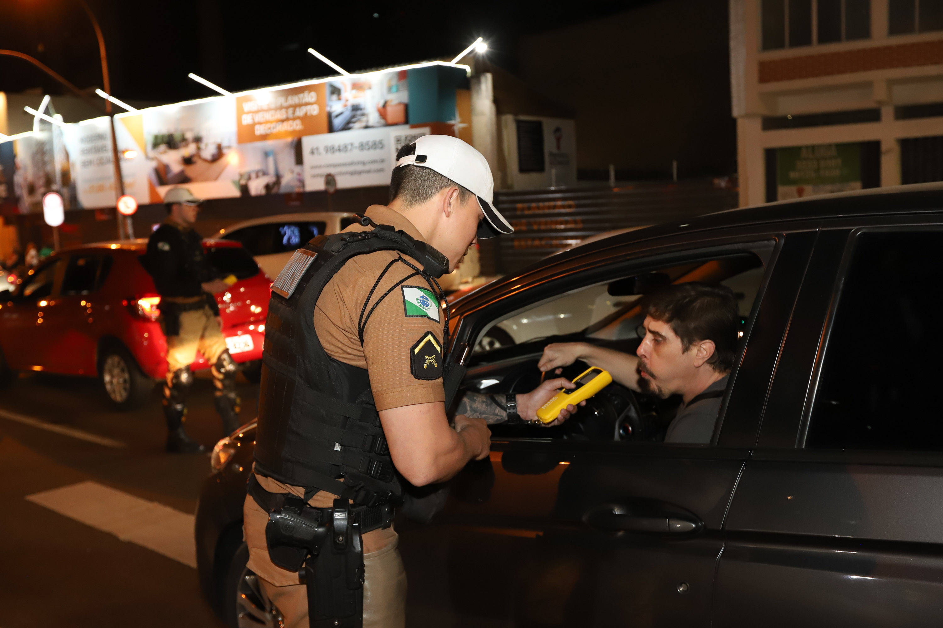 Agente realizando teste de alcoolemia em motorista durante fiscalização noturna.