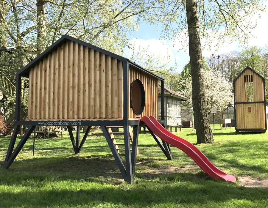 Cabane enfant Paris Copacabanon sur pilotis avec toboggan rouge dans un jardin au printemps