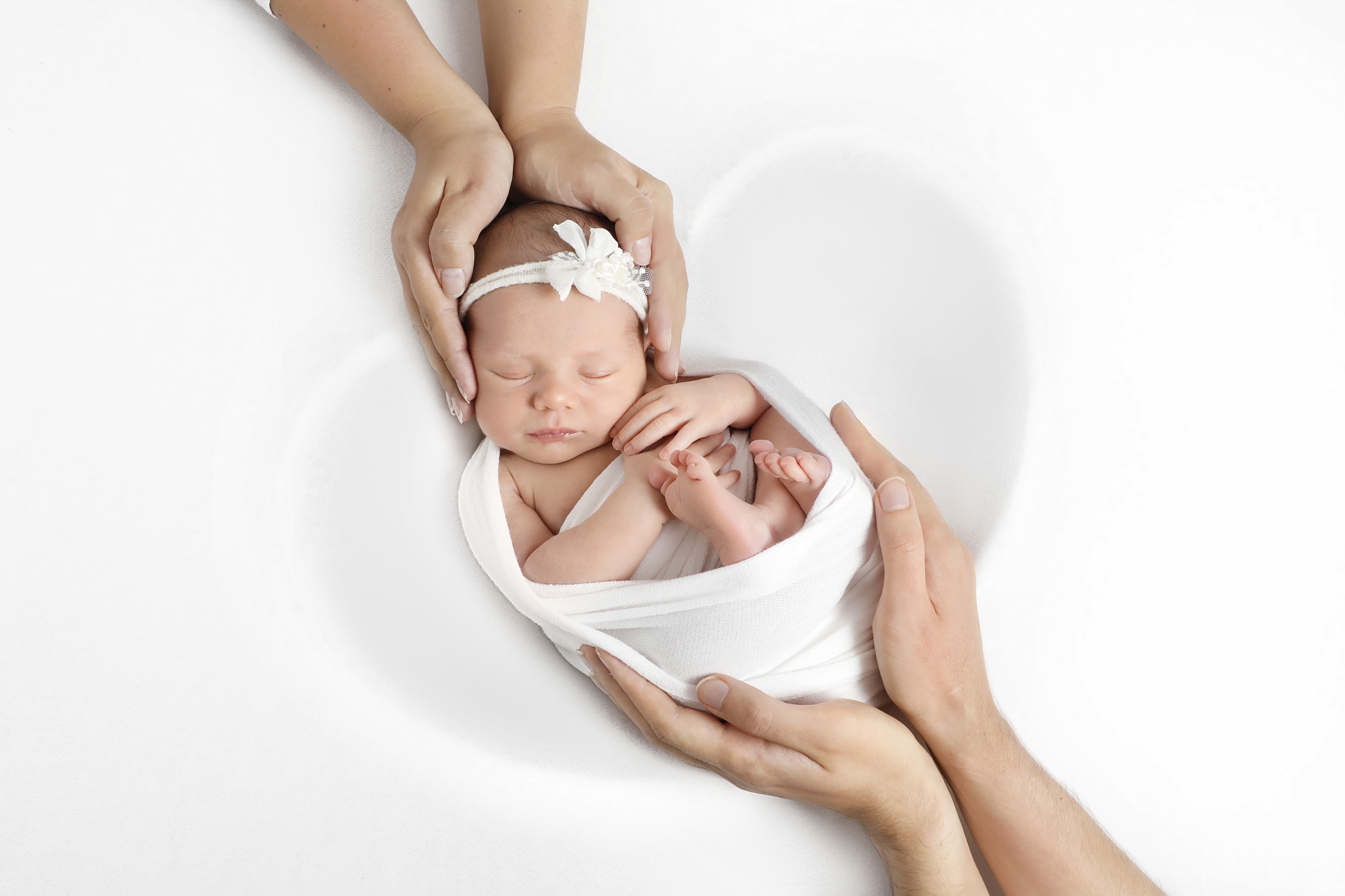 Top view of two pairs of hands safely holding the baby's head and limbs on opposite sides.
