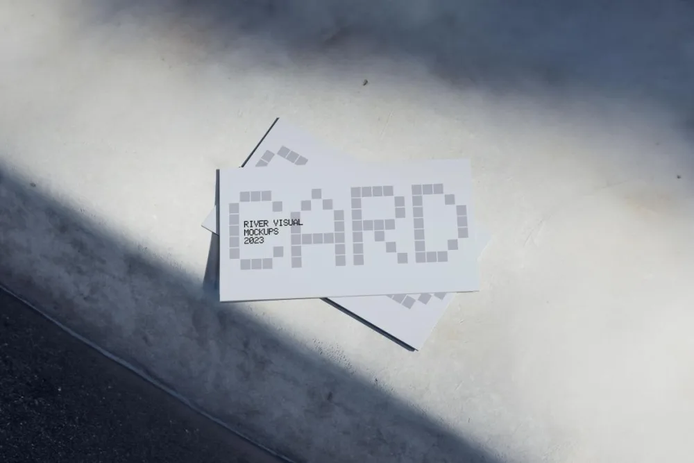 A stack of rectangular business card mockups displayed on a smooth, light gray concrete surface. The composition features natural shadowing, creating a minimalist and modern aesthetic.