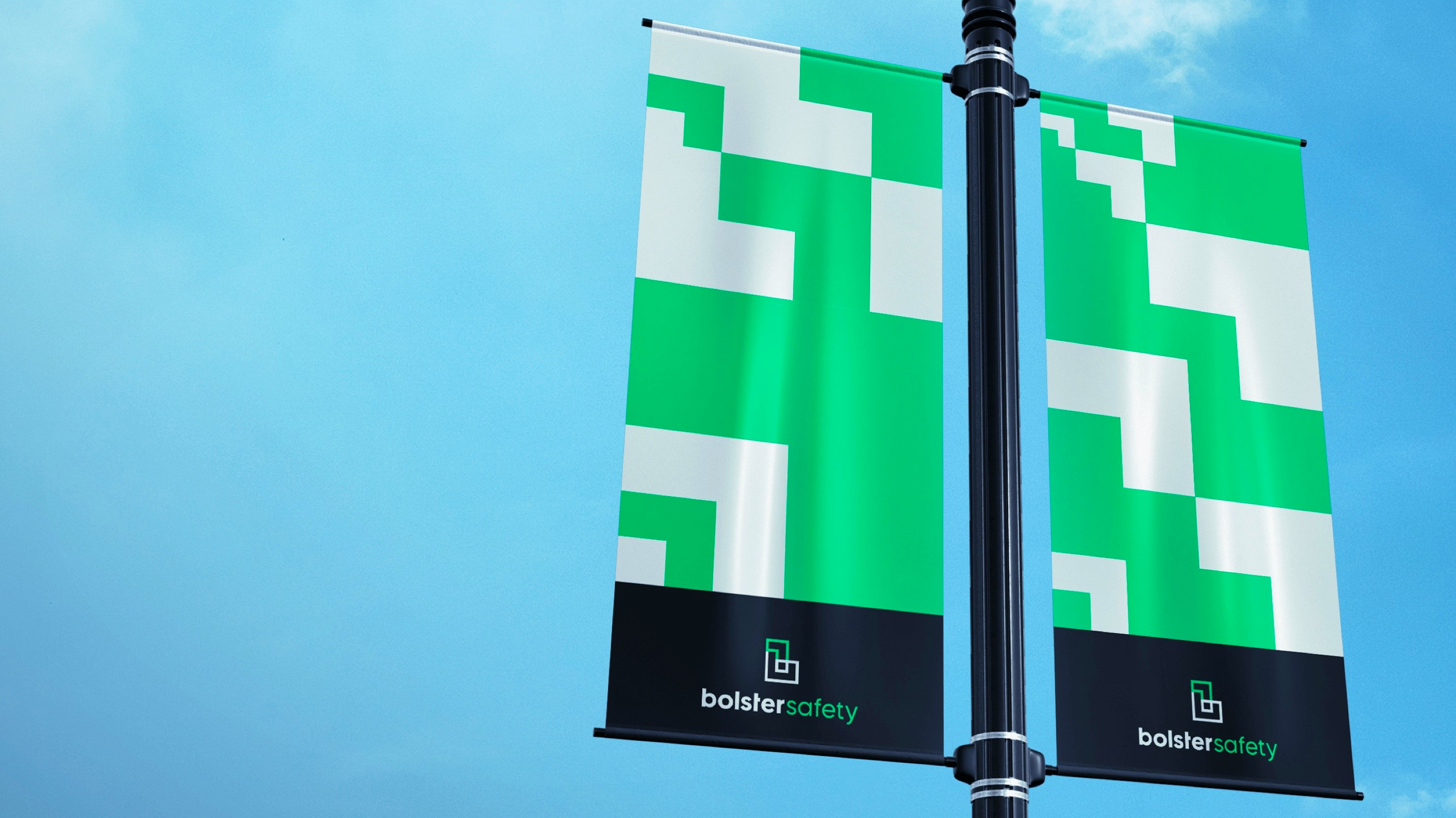 Bolster Safety — two Bolster Safety branded banners with a green and white geometric pattern hanging from a street lamp against a blue sky — Soda Studio case study