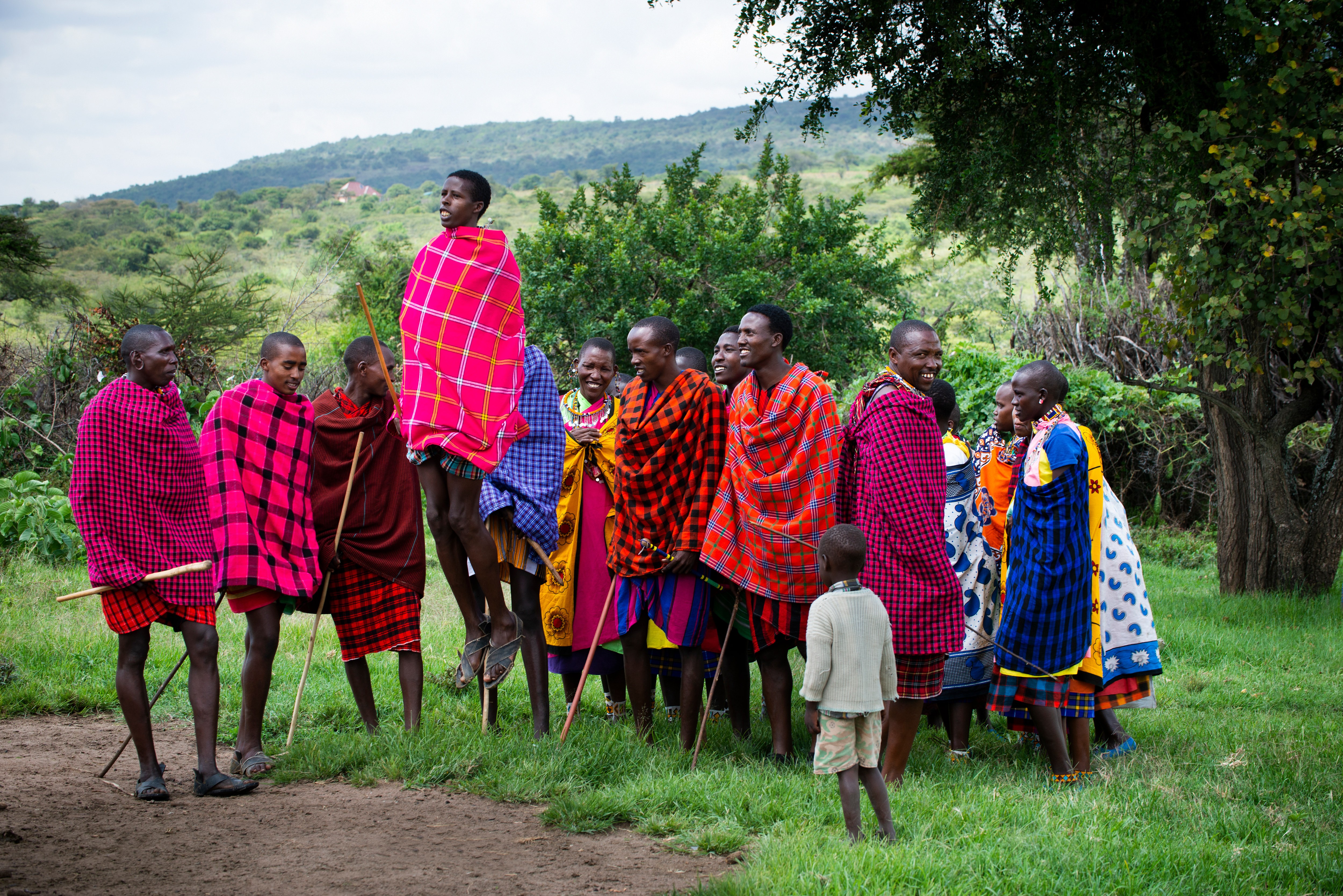 Maasai community members in colorful shukas gathered under a tree during a community visit