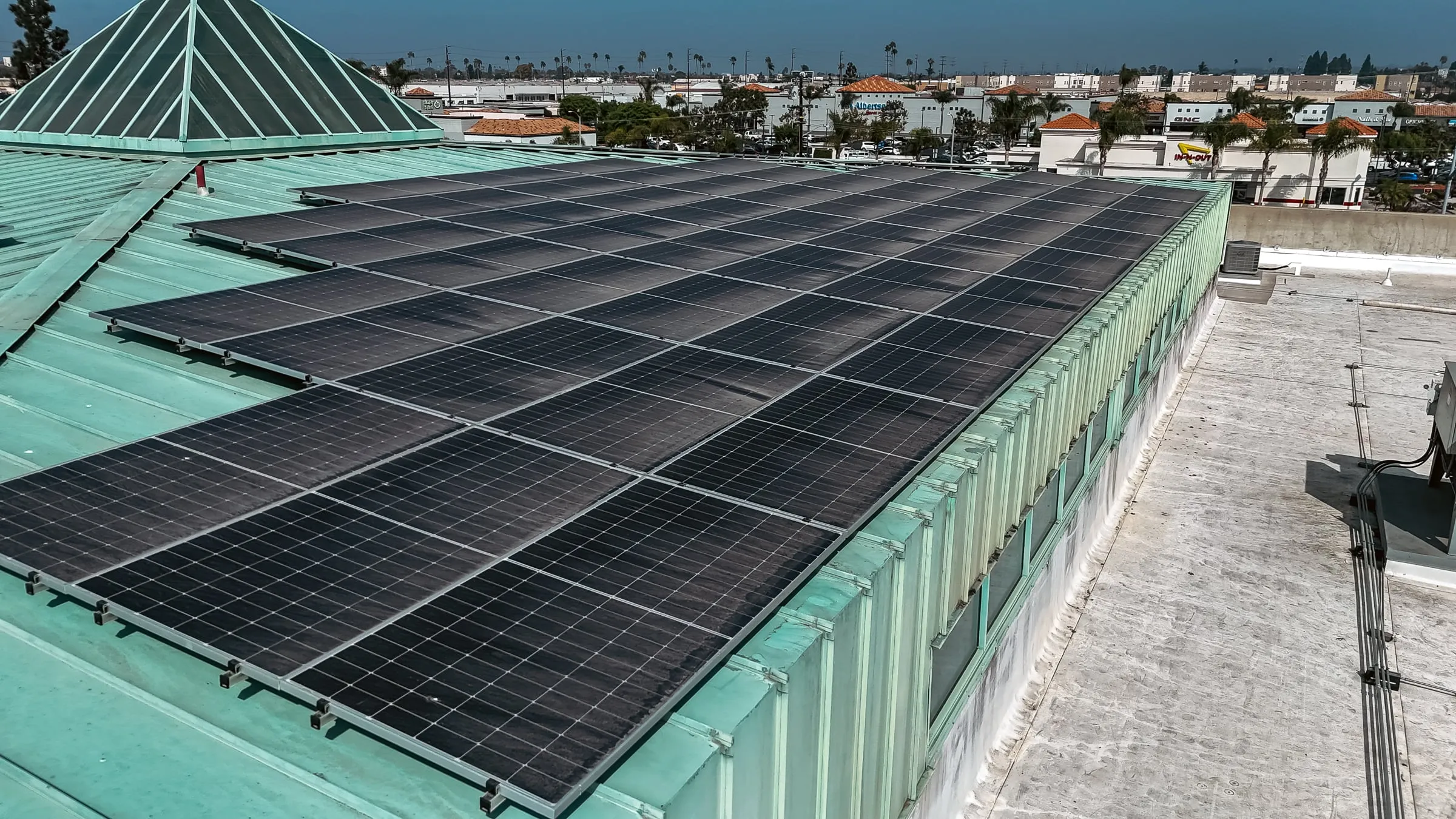 Close view of a solar array laid across a green metal commercial roof