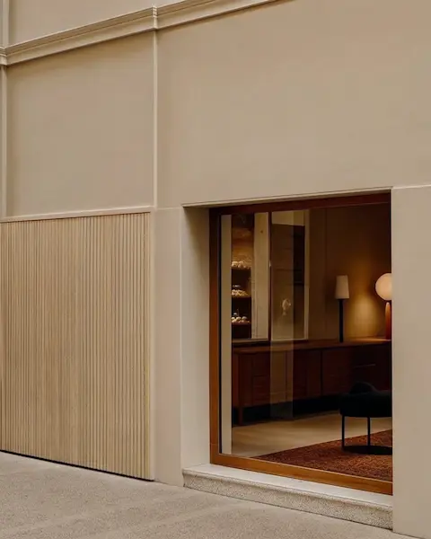 Esterno di un edificio minimalista con ingresso aperto che rivela un interno illuminato da luci calde, esempio di immobile di pregio.