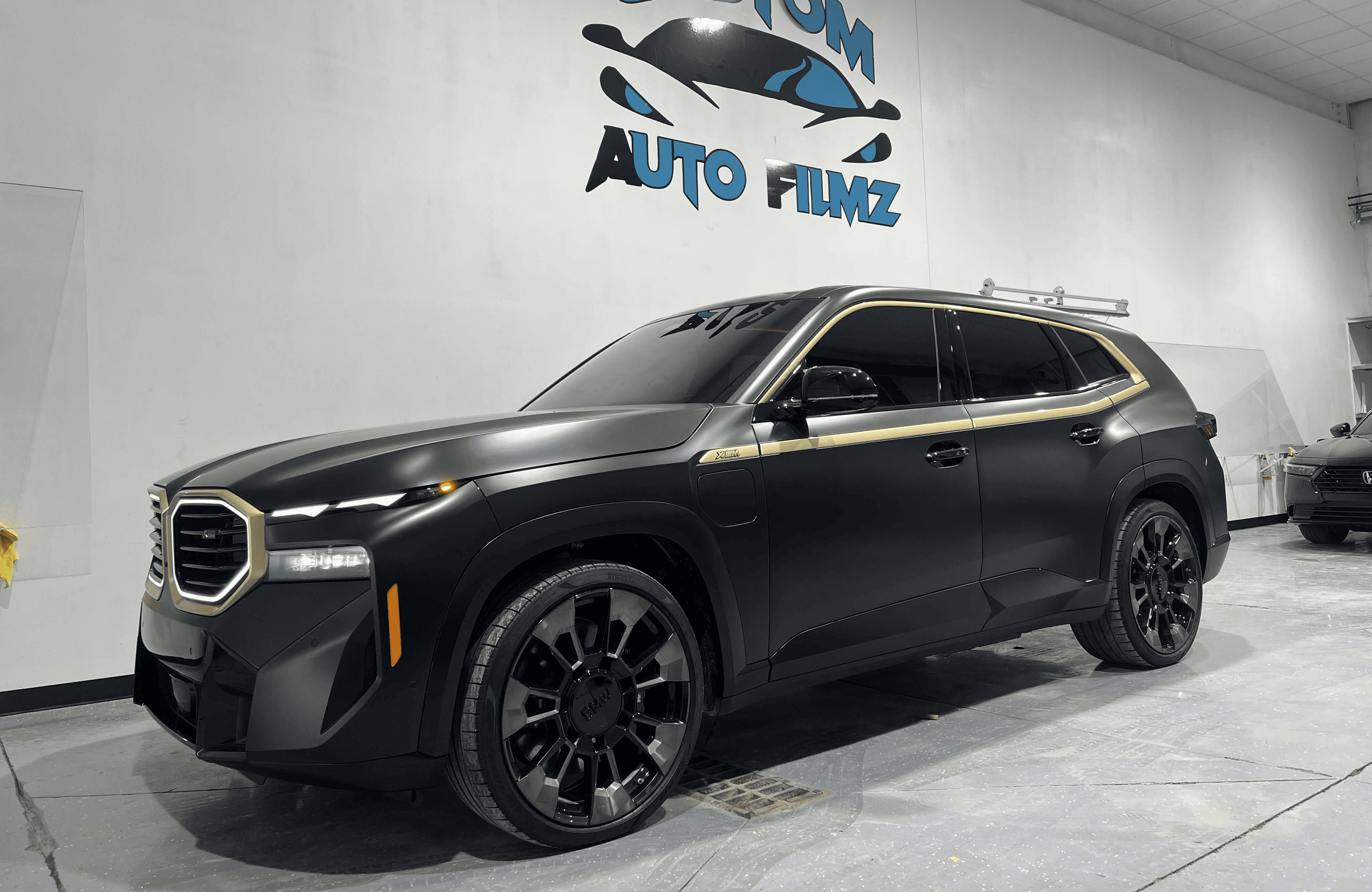 A matte black BMW XM luxury SUV is parked indoors on a polished concrete floor.