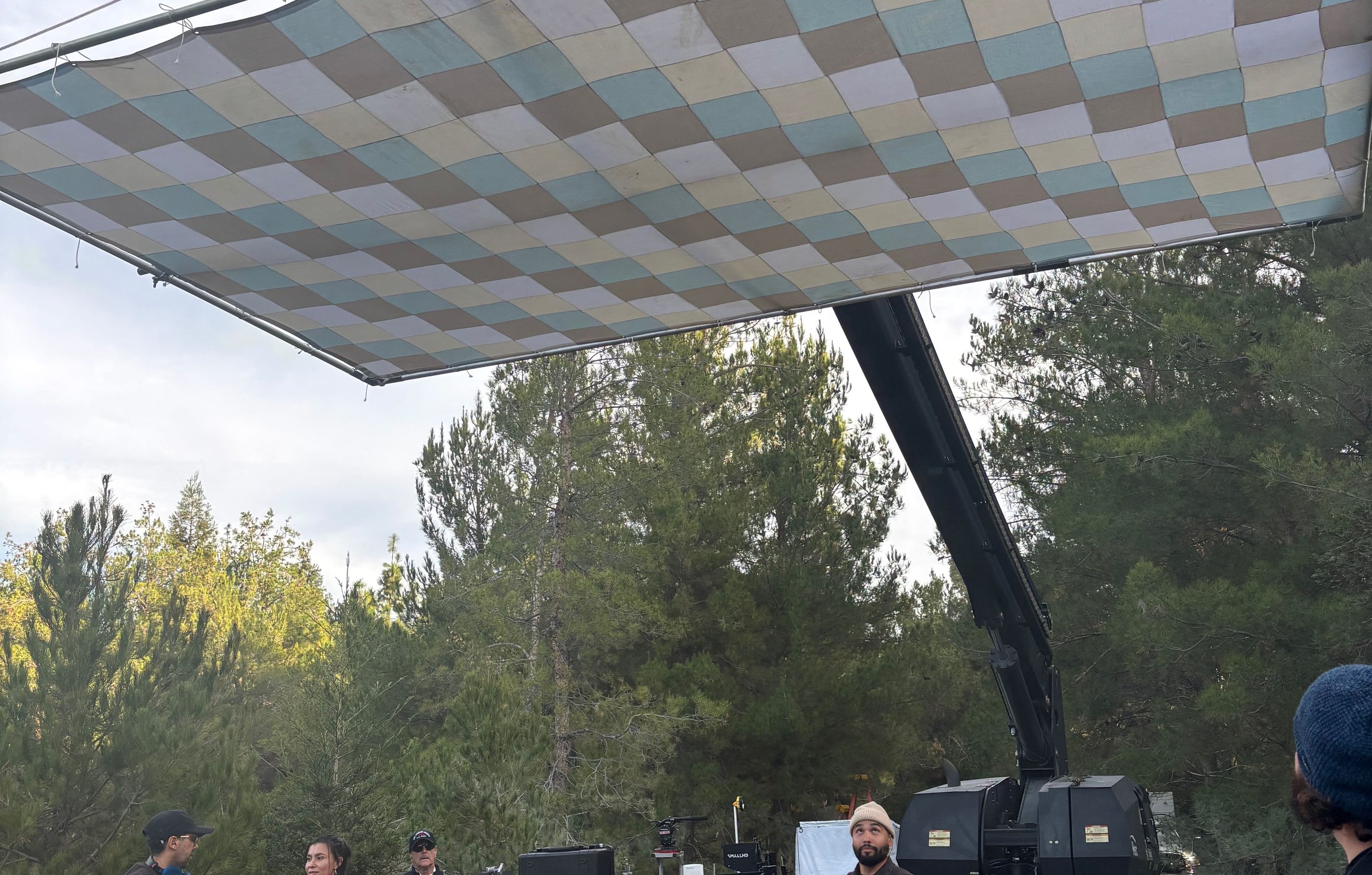 12x20 checker bounce flat overhead with two operators on top of the frame, crew on the dirt road below, Condor body visible at right.