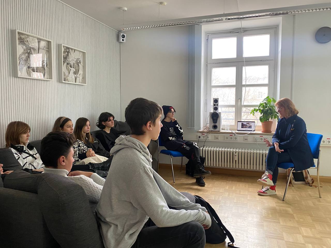 Junge Menschen sitzen auf Sofas und hören einem Dozenten aufmerksam zu.