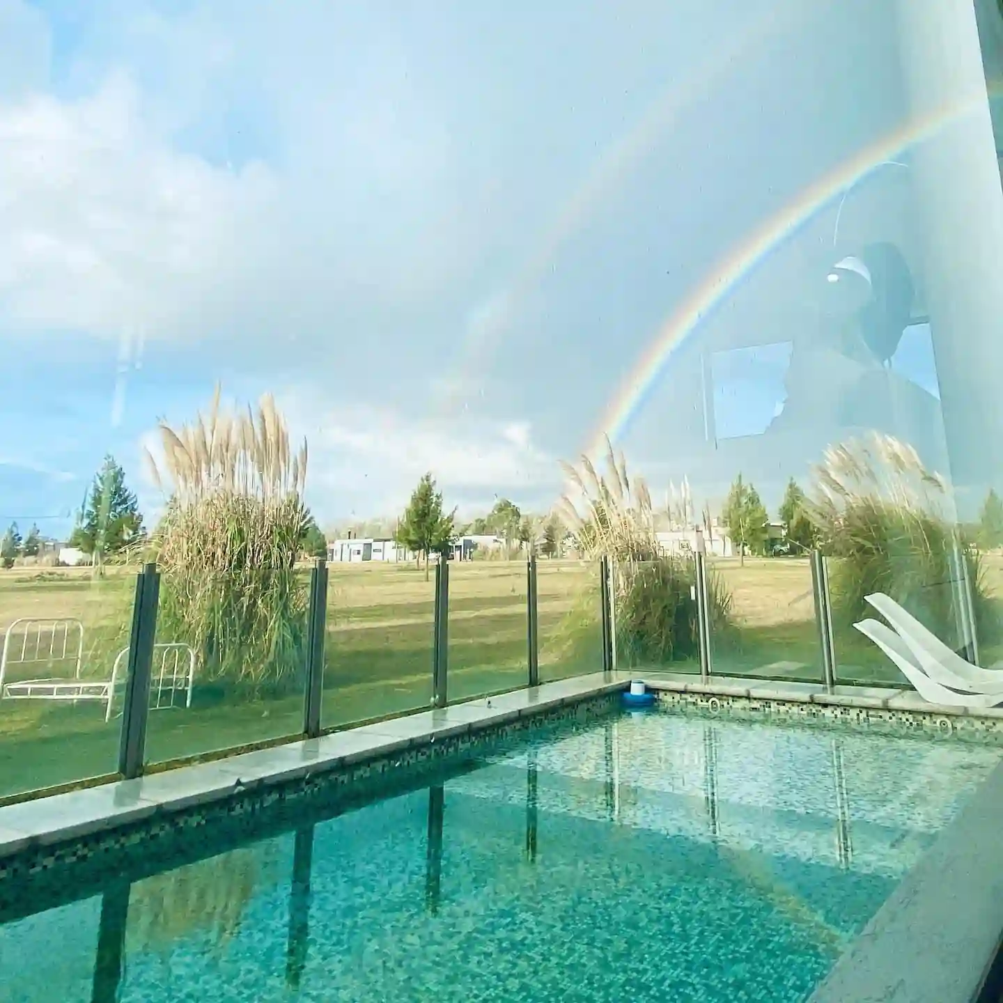 Pequeña pileta revestida en venecitas con cerco de vidrio perimetral de seguridad, con vista hacia un entorno abierto de barrio privado.