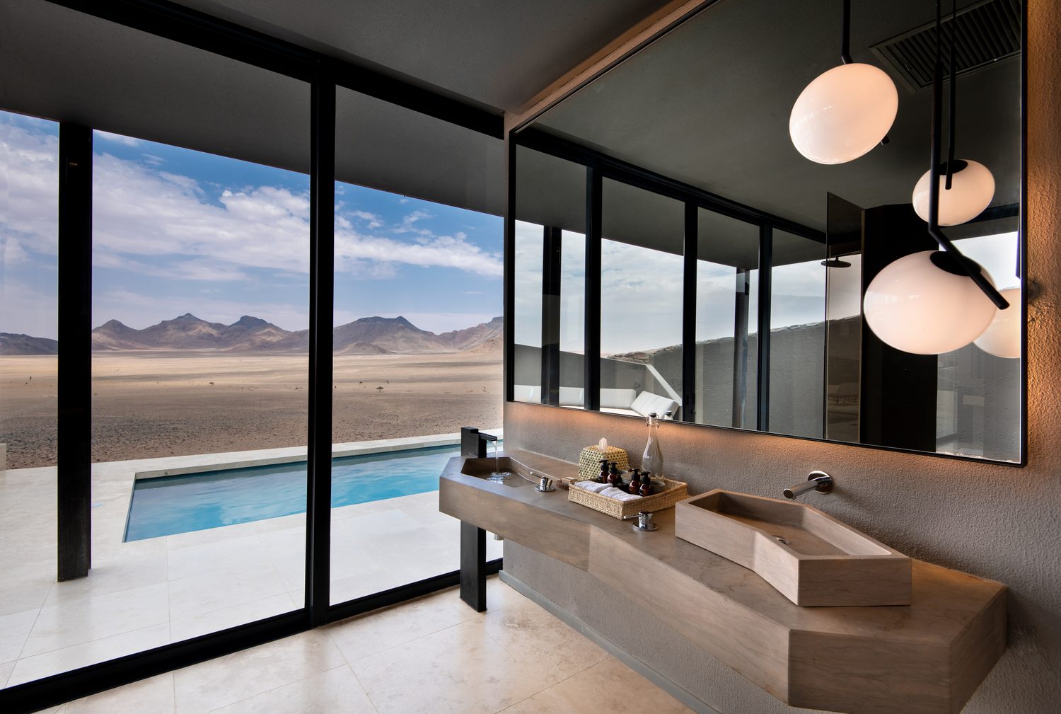 A desert-suite bathroom looking through glass walls to bare mountains
