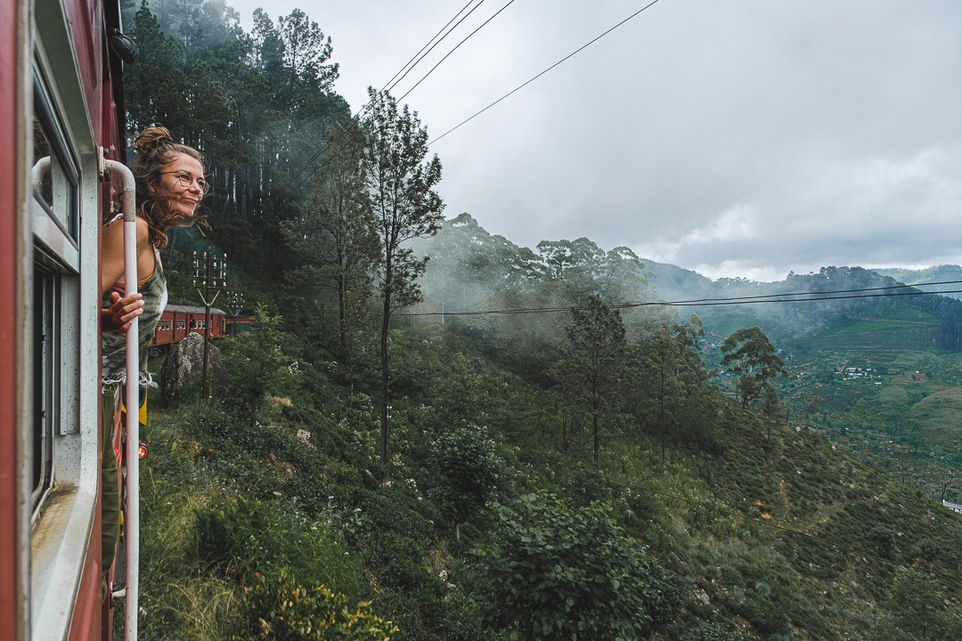 Eva leaning out of a train window surrounded by lush greenery.