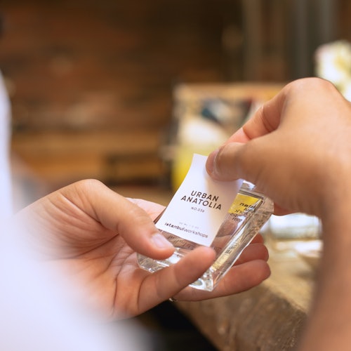 Isang kalahok ang naglalagay ng pasadyang label sa isang bote ng pabango na may label na "Urban Anatolia" habang nasa workshop.