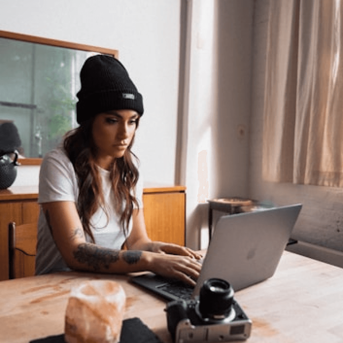 Woman working on a laptop computer at a table in a bright room.