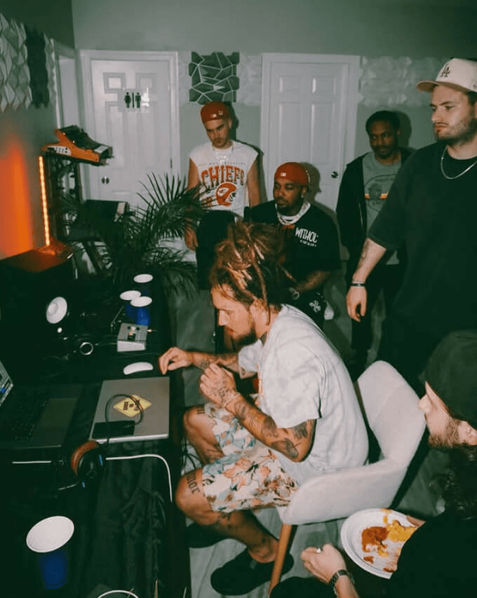 man making music on a laptop with other people watching in the background
