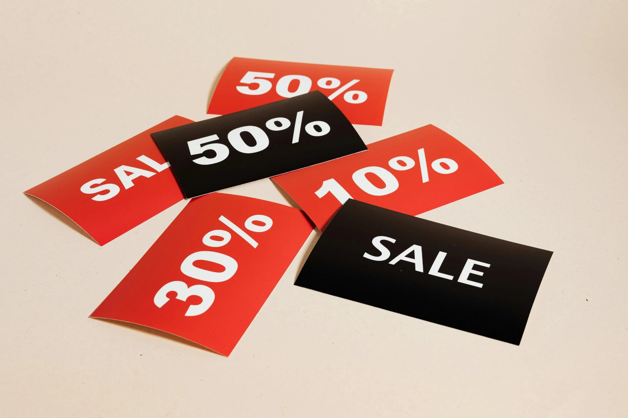 Red and black sale posters displaying "SALE," "10%," "30%," and "50%" discounts scattered on a light surface, conveying a promotional theme.