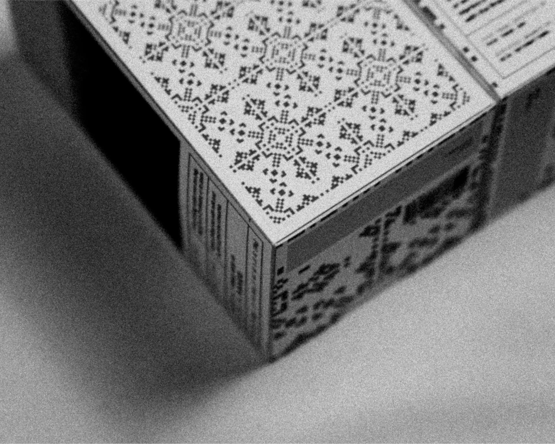 A close-up shot of a monochrome, patterned box featuring intricate geometric designs in a lace-like motif, positioned on a soft, white surface.