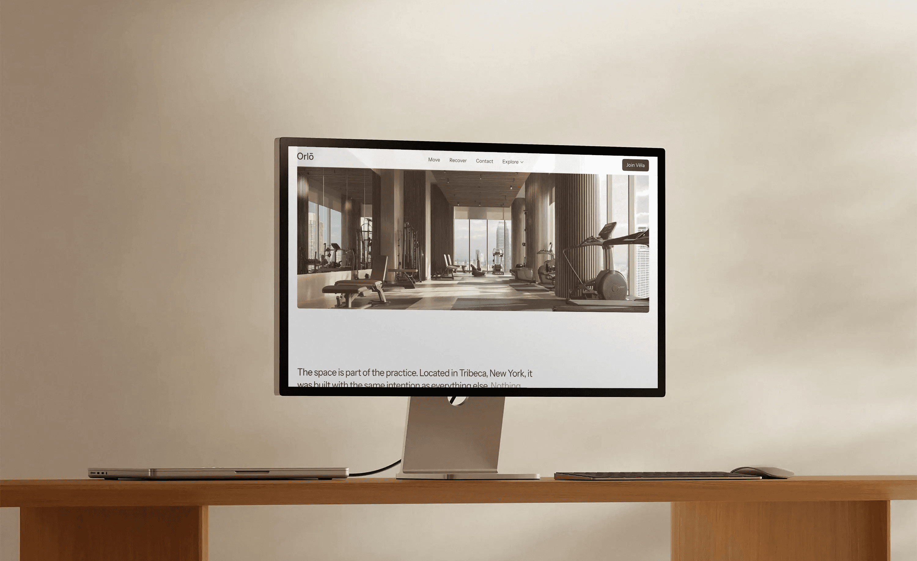 Desktop monitor on a wooden desk displaying the Orlō website with a sunlit Tribeca fitness studio
