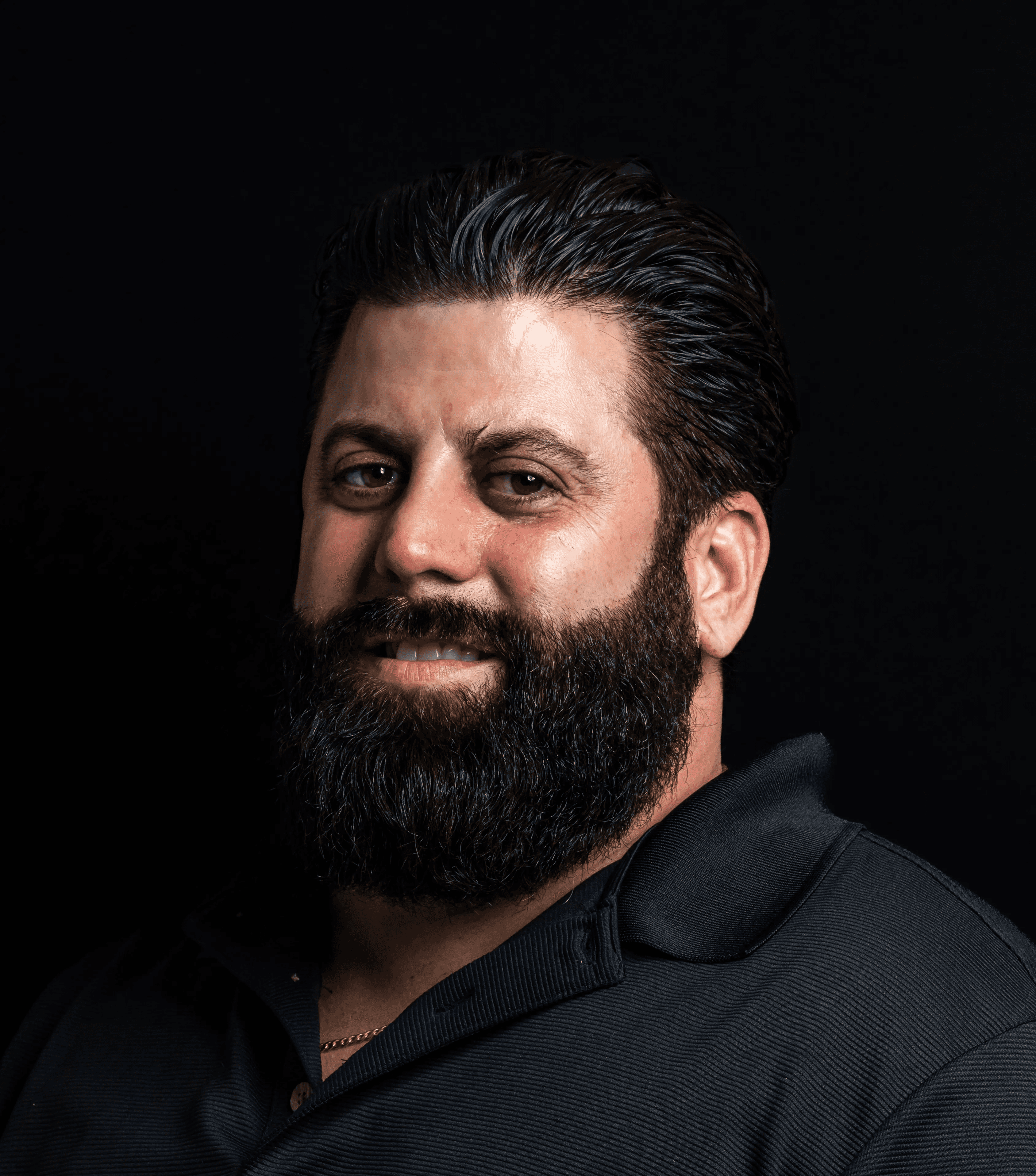 Man with a beard smiling against a black background.