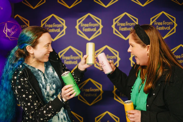 Two people smiling with multiple Cans products infront of the free from festival photowall