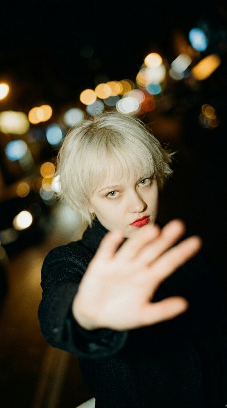 Candid night portrait of a woman reaching toward the camera with city lights