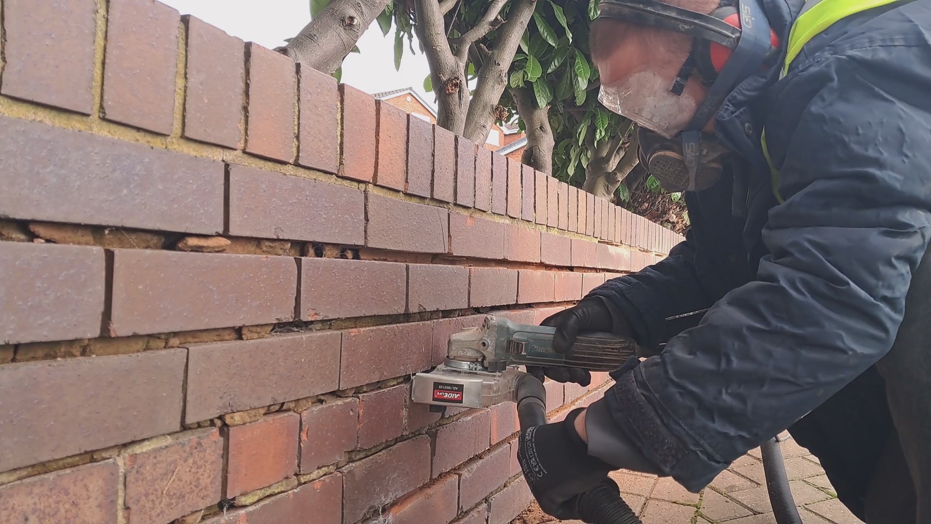 A man grinding out mortart from a garden wall