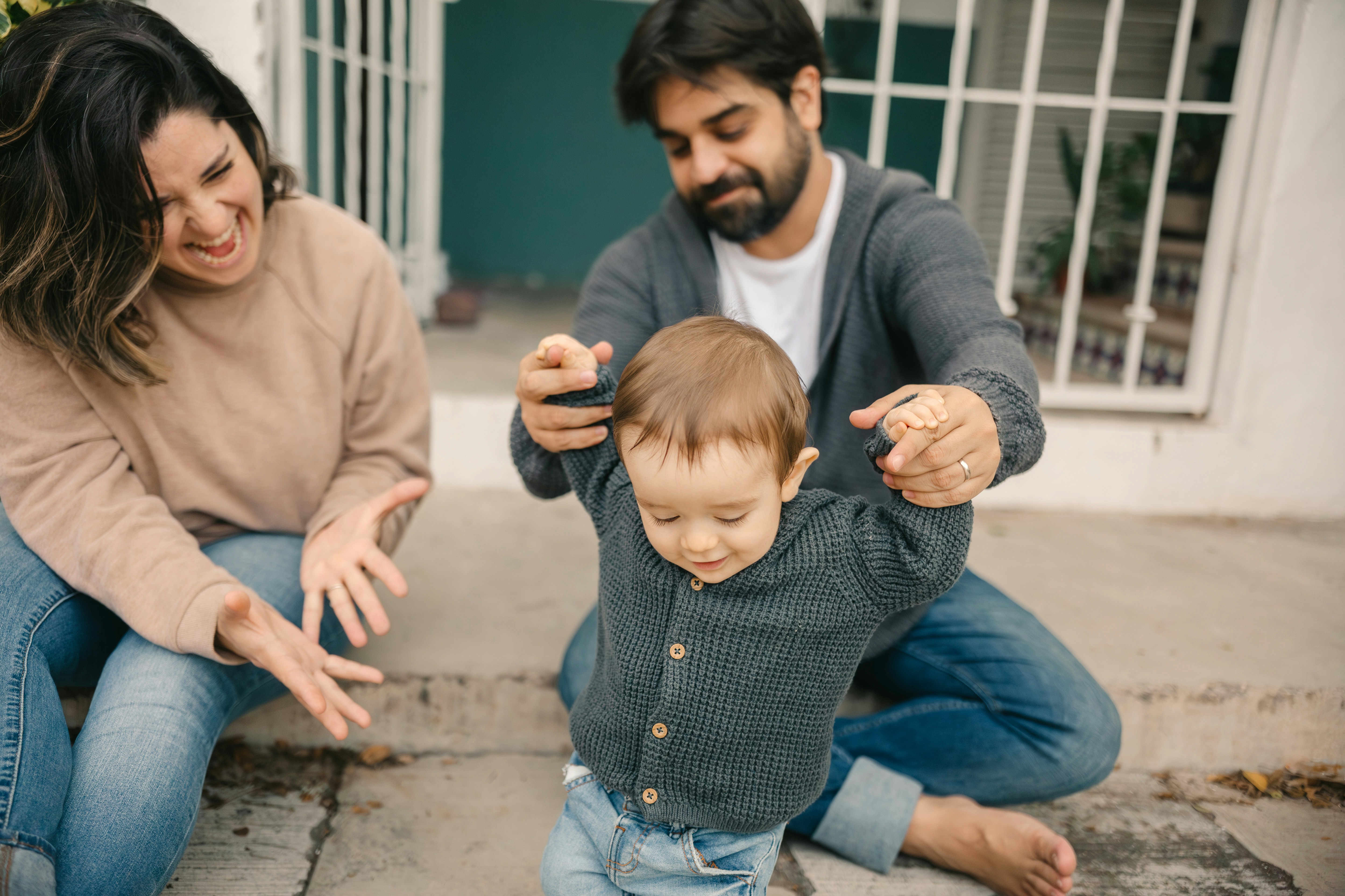 parents helping toddler as he learns to walk